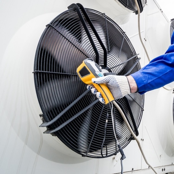 Large air conditioner fan with HVAC repairman holding an infrared thermometer.