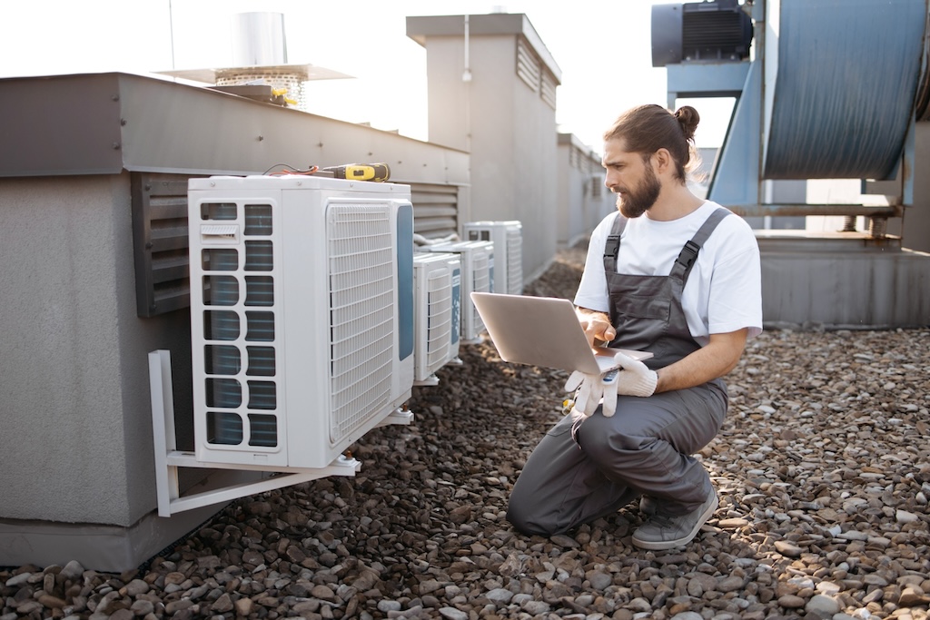 HVAC technician with laptop for diagnostics on commercial roof.